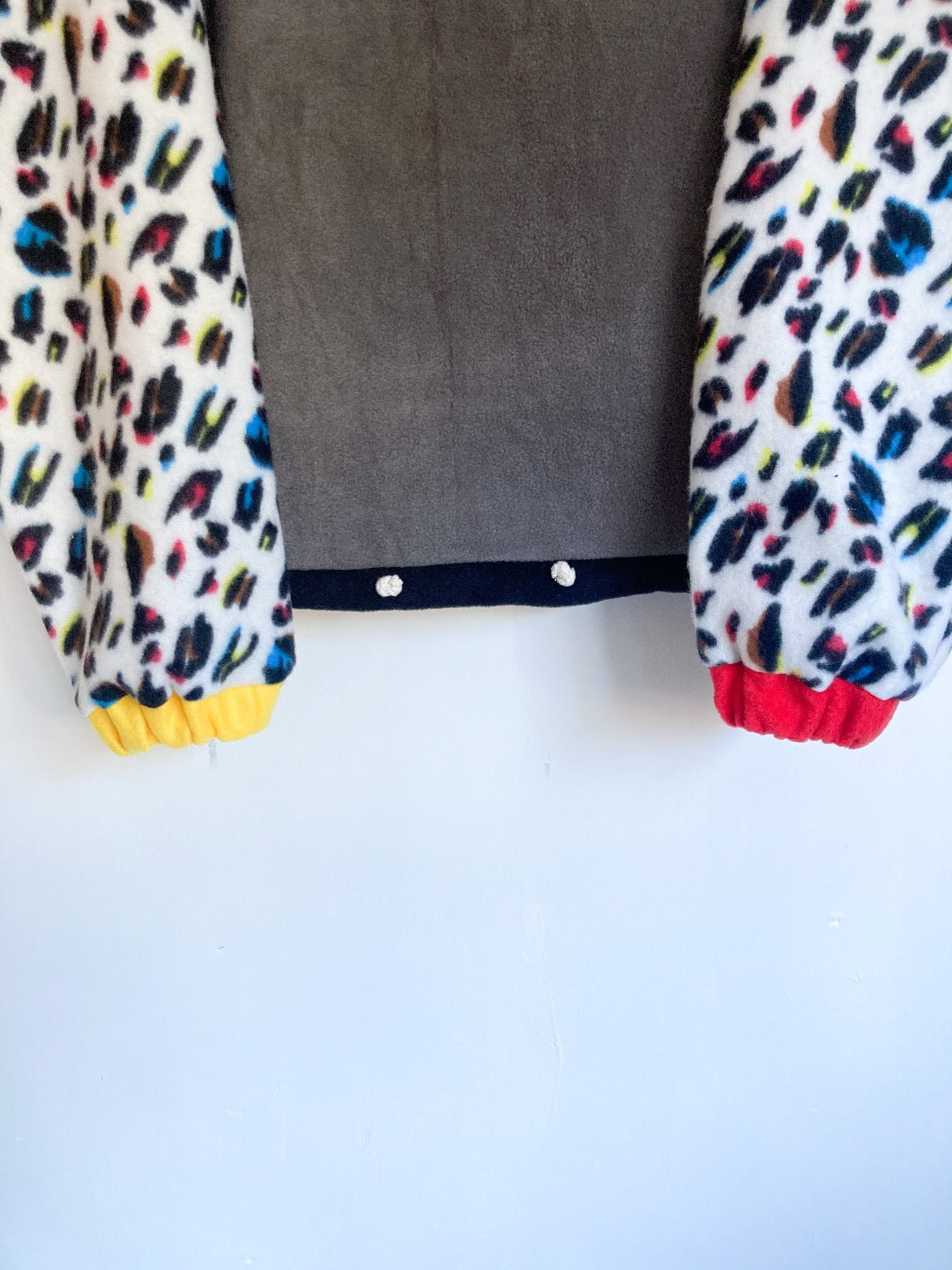 Grey fleece with black trim, white leopard print sleeves and alternate yellow and red cuffs. 